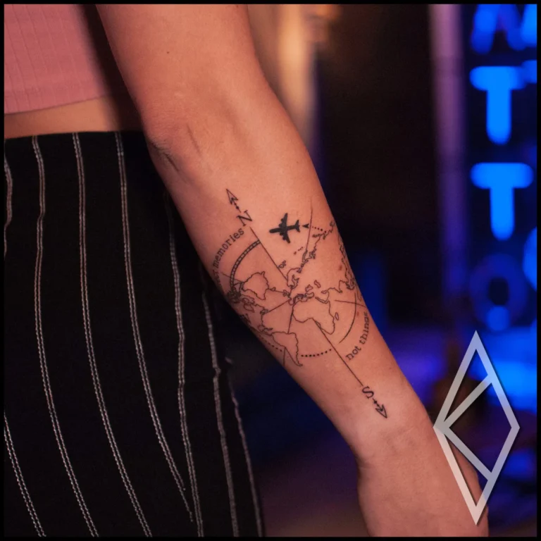 Compass with world map and an airplane flying over tattoo on forearm